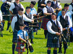 A young boy playing bagpipe with adults